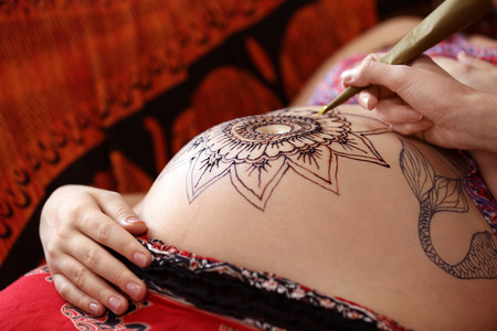 Tattoo master drawing henna tattoo on pregnant belly, closeupの写真素材