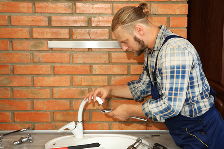 Handsome plumber repairing faucet in kitchenの写真素材