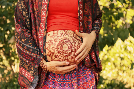 Young pregnant woman with henna tattoo on belly in parkの写真素材