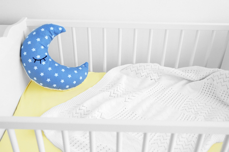 White crib with plaid and half moon cushion, close up view
