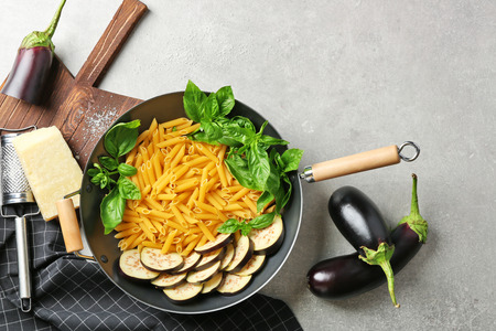 Pan with ingredients for tasty pasta, napkin, kitchen board and grater on grey table, top viewの写真素材