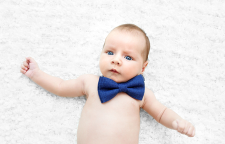 Cute baby with bow tie lying on white bedspreadの写真素材