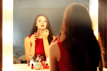 Beautiful girl applying cosmetics in front of mirrorの写真素材
