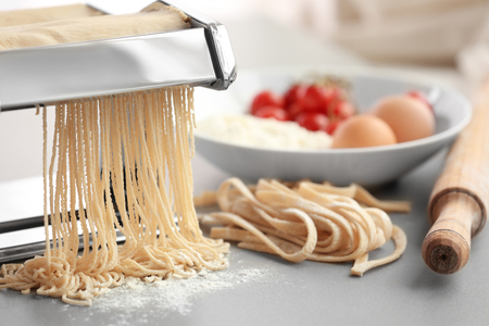 Making tagliatelle with pasta machine on kitchen tableの写真素材