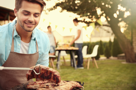 Handsome young man preparing barbecue steaks on grillの写真素材