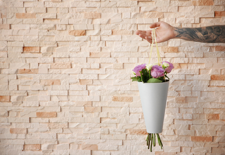 Male hand holding beautiful bouquet on blurred brick wall backgroundの写真素材