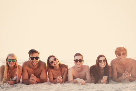 Happy friends lying on beach sandの写真素材