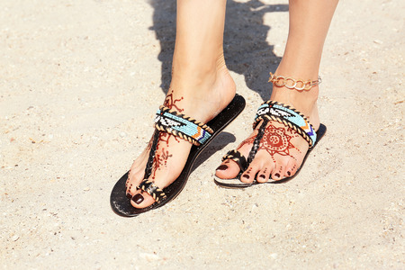 Female legs with henna tattoo on beach sand background