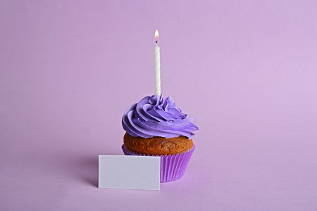 Fresh tasty cupcake with candle and birthday card on lilac backgroundの写真素材