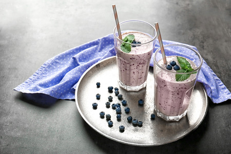Tray with two glasses of tasty smoothie, blueberries and straws on grey tableの写真素材