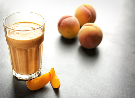 Glass with tasty smoothie and peach on grey tableの写真素材