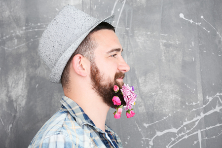 Handsome man in hat with beard of flowers on light backgroundの写真素材