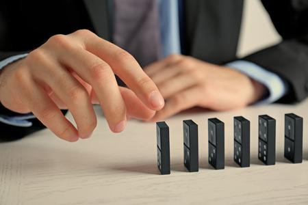 Businessman hand trying to toppling dominoes on tableの写真素材