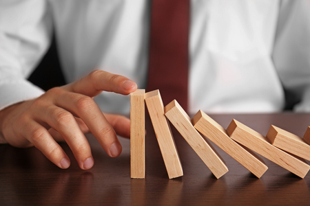 Businessman hand trying to stop toppling dominoes on tableの写真素材