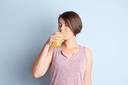 Young beautiful woman with glass of orange juice, on light backgroundの写真素材