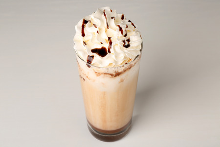 Glass of delicious milk shake with whipped cream and chocolate topping on light backgroundの写真素材