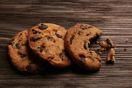 Tasty cookies with chocolate chips and crumbs on wooden background