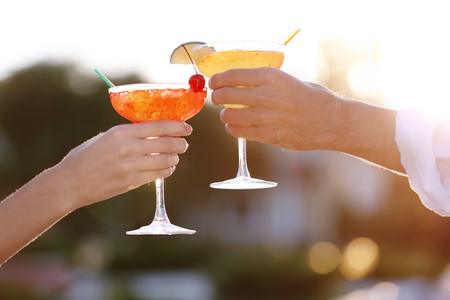 Male and female hands holding glasses with margarita cocktail on blurred backgroundの写真素材