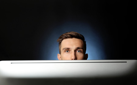 Man sitting at computer monitor on dark backgroundの写真素材