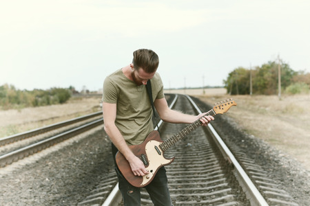Handsome man with guitar on railroadの写真素材