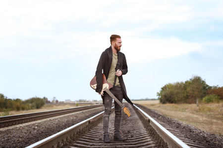 Handsome man with guitar on railroadの写真素材