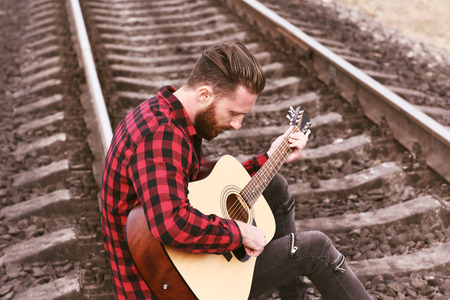 Handsome man playing guitar on railroadの写真素材