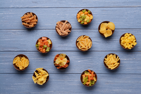 Different kinds of pasta in bowls on wooden backgroundの写真素材