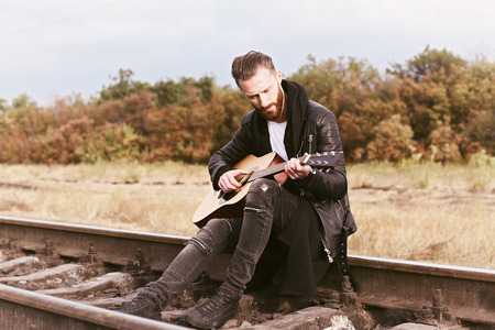 Handsome man playing guitar on railroad
