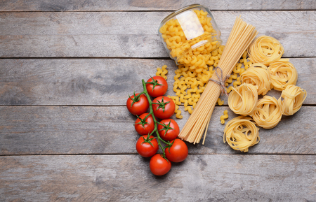 Different kinds of pasta and tomatoes on wooden backgroundの写真素材