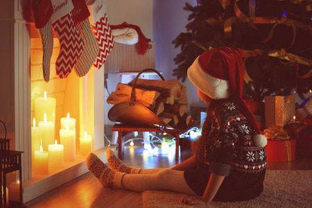 Little girl sitting near fireplace decorated for Christmasの写真素材