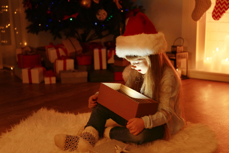 Little girl opening Christmas present in living roomの写真素材