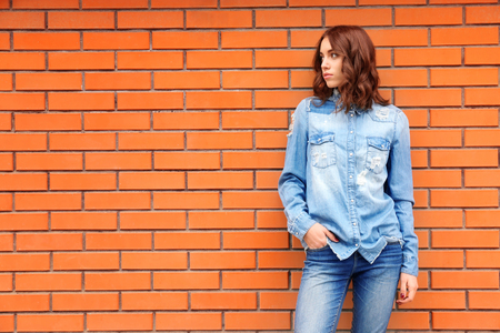 Young woman in casual clothes standing against brick wallの写真素材