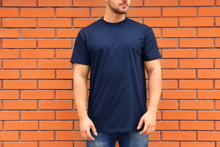 Young man in blank t-shirt standing against brick wall, closeup