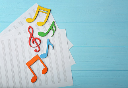 Music notes and sheets of paper on color wooden background