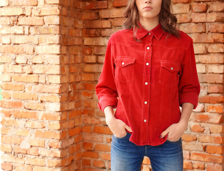 Young woman in casual clothes standing against brick wall, closeup