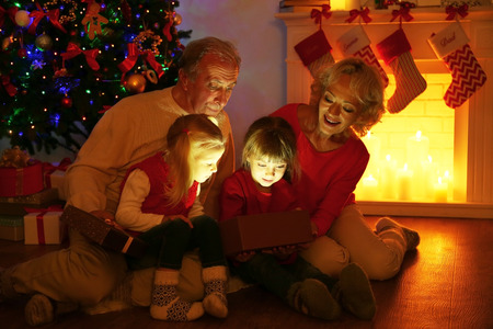 Elderly couple with their granddaughters opening Christmas present near fireplaceの写真素材