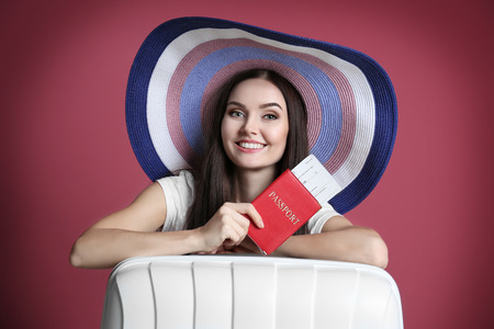 Young beautiful woman with suitcase holding passport on purple backgroundの写真素材