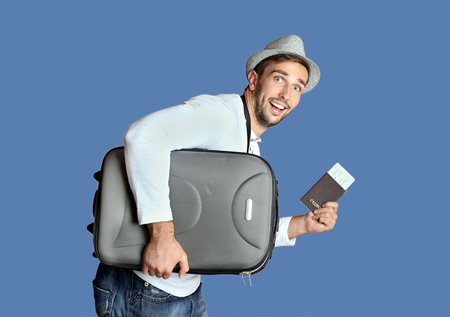 Young man with suitcase and ticket on blue backgroundの写真素材