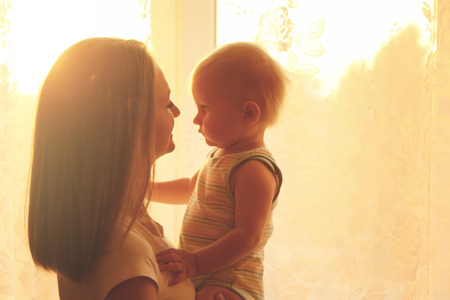 Mother with cute child near window at homeの写真素材