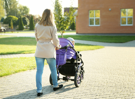 Woman with baby stroller walking in green park