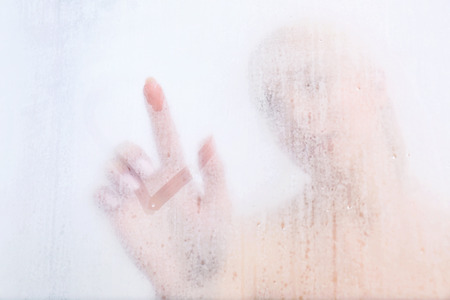 Beautiful young woman drawing on weeping glass of  shower doorの写真素材