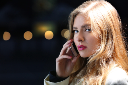 Young woman talking on smart phone in street at eveningの写真素材