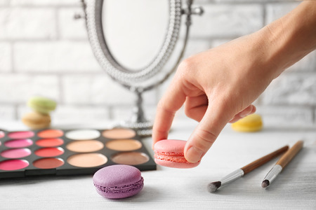Woman holding macaroon above beauty accessories on tableの写真素材