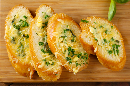 Tasty bread with garlic, cheese and herbs on wooden kitchen board, close upの写真素材