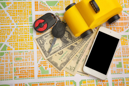 Yellow toy taxi, car key and phone with money on map