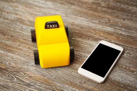 Yellow toy taxi with phone on wooden background
