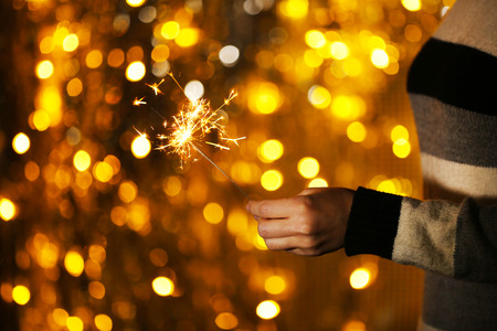 Woman holding sparkler against defocused lights, close up