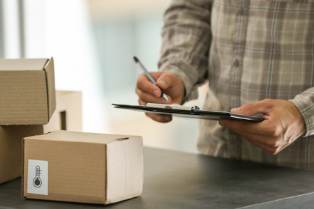 Courier making notes in delivery receipt at tableの写真素材