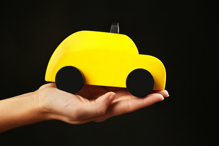 Woman holding yellow toy taxi on black backgroundの写真素材