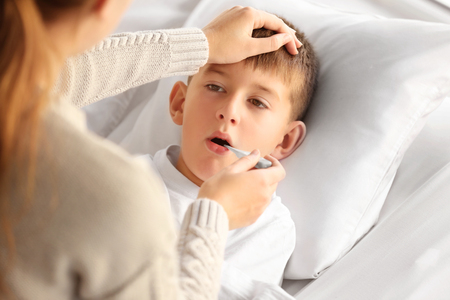 Small sick boy with thermometer in bedの写真素材